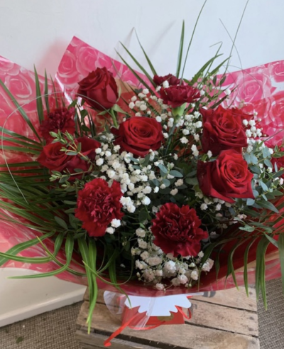 Smooch - A hand tied bouquet 6 long stem large red roses and 6 deep red carnation with pretty white gyp and lush foliage throughout. Presented in red wraps and a red box.